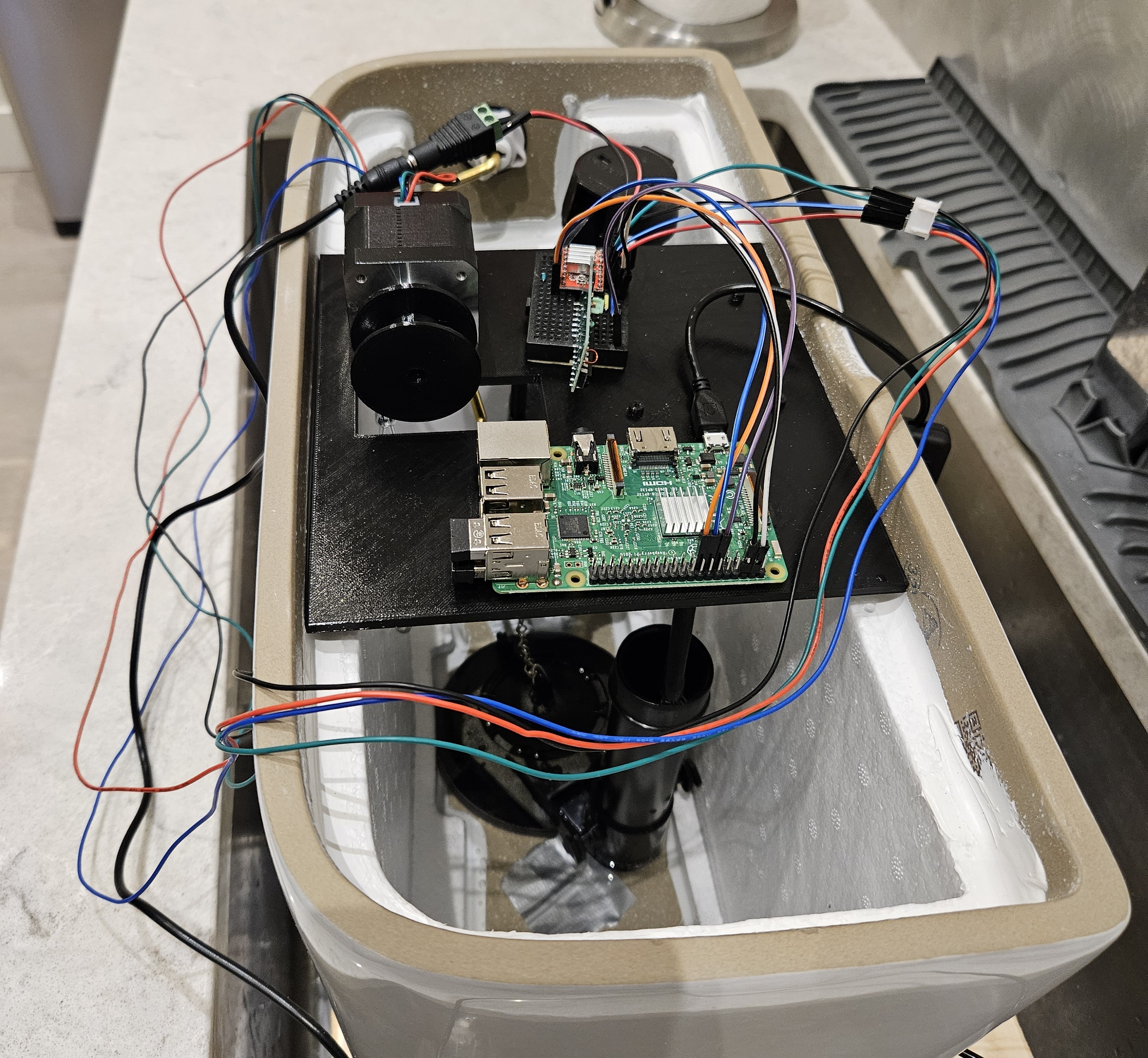 A Raspberry Pi inside the top of a toilet tank, with wires sprawled everywhere and a motor linked to the flush chain.