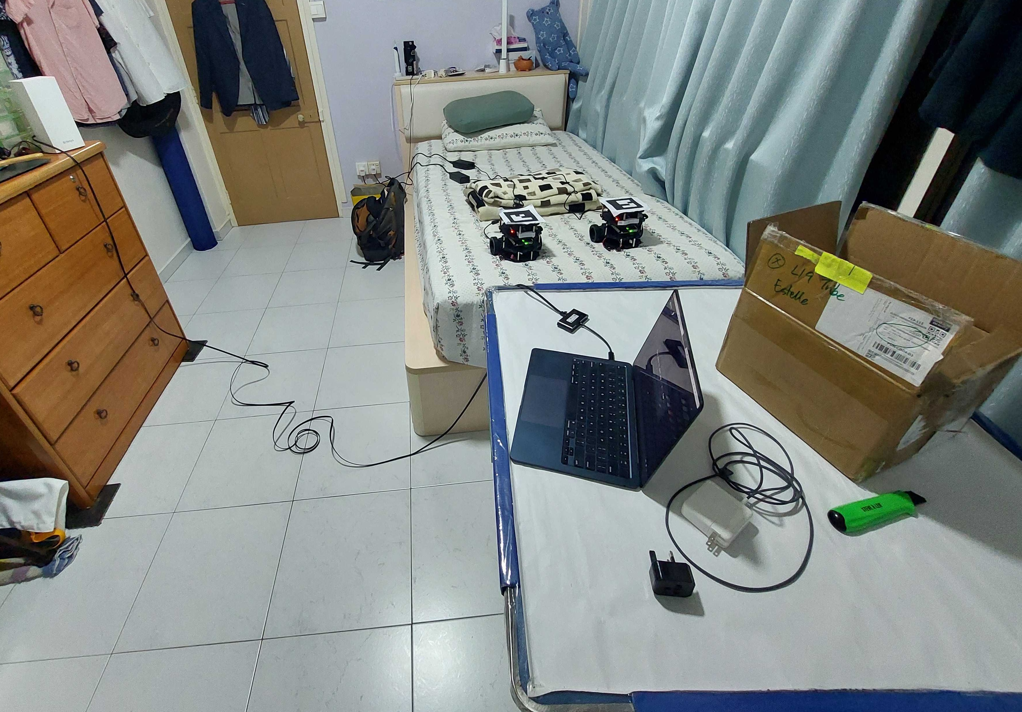 My room while I was in Singapore for the competition. A router is placed on top of a dresser on one side of the room, while two robots rest on my bed on the other side. My laptop is sitting on top of a Mahjong table, which I am using as a desk.